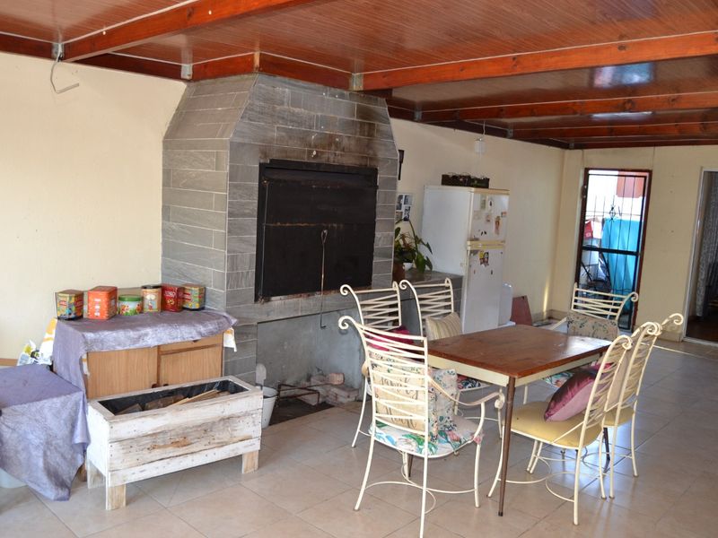 Covered patio area featuring a built-in stone-clad braai, exposed timber beam ceiling, and tiled flooring, providing a functional space for outdoor entertaining.