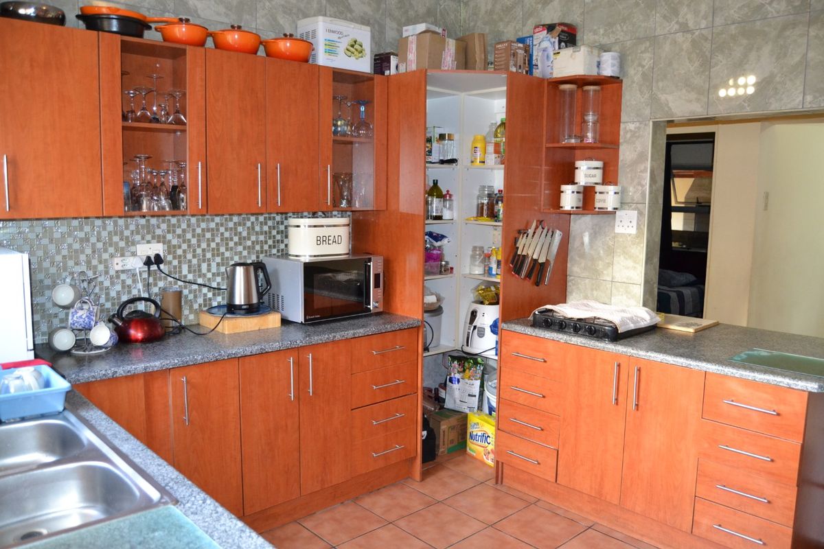 Functional kitchen featuring wood-look cabinetry, granite countertops, a double stainless steel sink, and integrated pantry storage with tiled finishes throughout.
