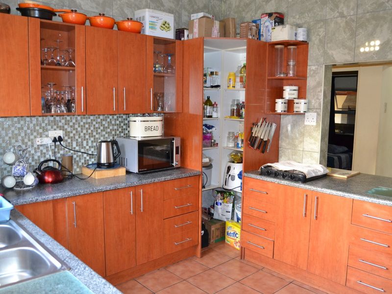 Functional kitchen featuring wood-look cabinetry, granite countertops, a double stainless steel sink, and integrated pantry storage with tiled finishes throughout.