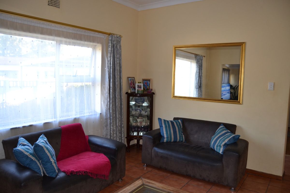 A living room featuring tiled flooring, neutral wall paint, and a large wall-mounted mirror, providing a functional and well-lit space.