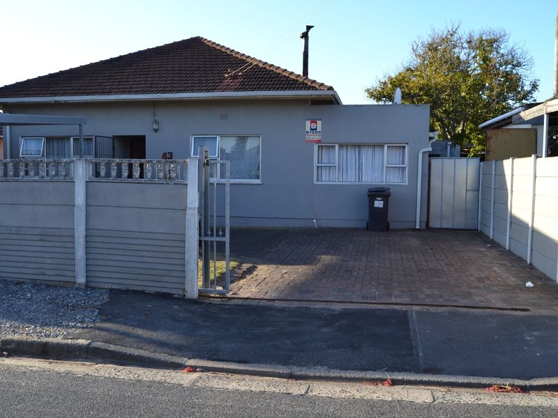 Front elevation of a single-story house featuring a tiled roof, paved driveway, and secure boundary walling with a metal gate.