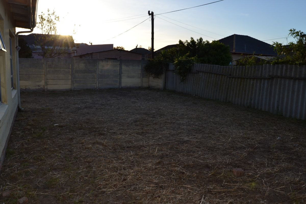 A spacious rear garden area featuring a mix of precast concrete and corrugated metal boundary fencing, offering a blank canvas for landscaping.
