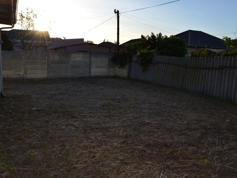 A spacious rear garden area featuring a mix of precast concrete and corrugated metal boundary fencing, offering a blank canvas for landscaping.