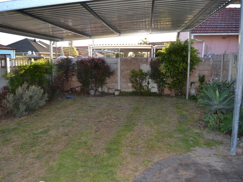 A covered outdoor patio area featuring a corrugated metal roof, paved flooring, and a private garden space enclosed by precast concrete walls.