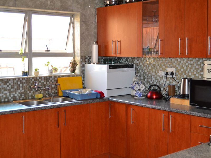 A functional kitchen featuring warm-toned laminate cabinetry, granite countertops, a double basin sink, and a decorative mosaic tile backsplash.
