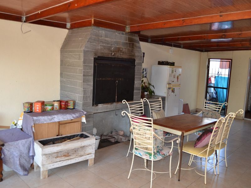 Covered patio area featuring a built-in braai, tiled flooring, and exposed timber beam ceiling, providing a functional space for outdoor dining and entertainment.