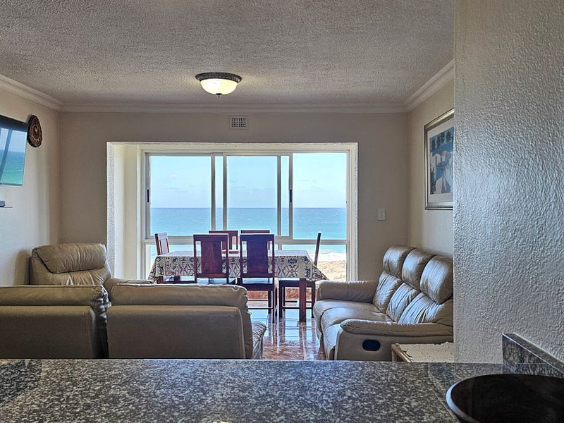Open plan living and dining area featuring tiled flooring, granite kitchen counter, and large sliding glass doors with direct ocean views.