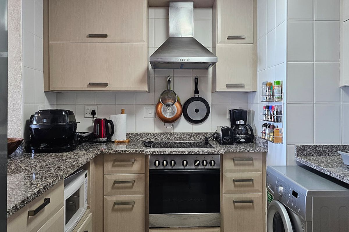 A functional kitchen featuring light wood cabinetry, granite countertops, a stainless steel extractor fan, and a built-in oven with a ceramic hob.