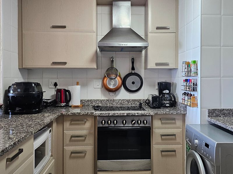 A functional kitchen featuring light wood cabinetry, granite countertops, a stainless steel extractor fan, and a built-in oven with a ceramic hob.