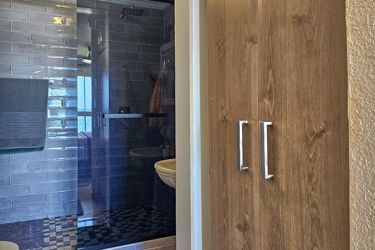 A modern bathroom featuring a glass-enclosed shower with subway tiling, mosaic floor accents, and integrated wooden cabinetry for storage.