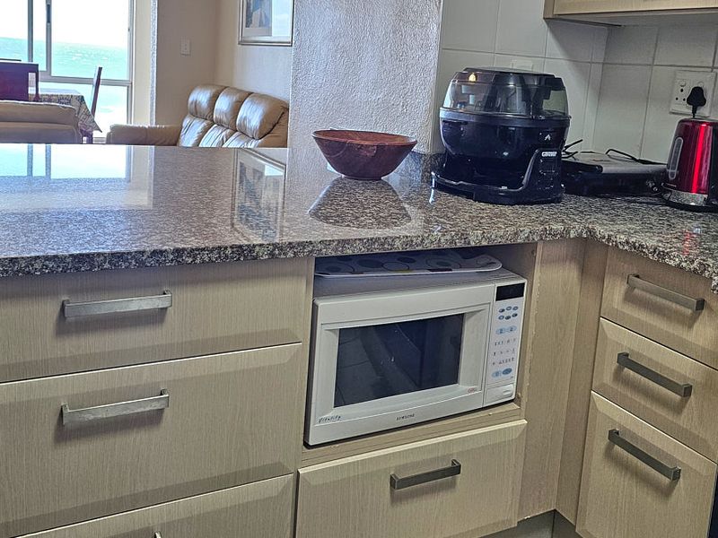 A functional kitchen featuring granite countertops, light wood-finish cabinetry, and built-in appliances, with an open-plan layout connecting to the living area.