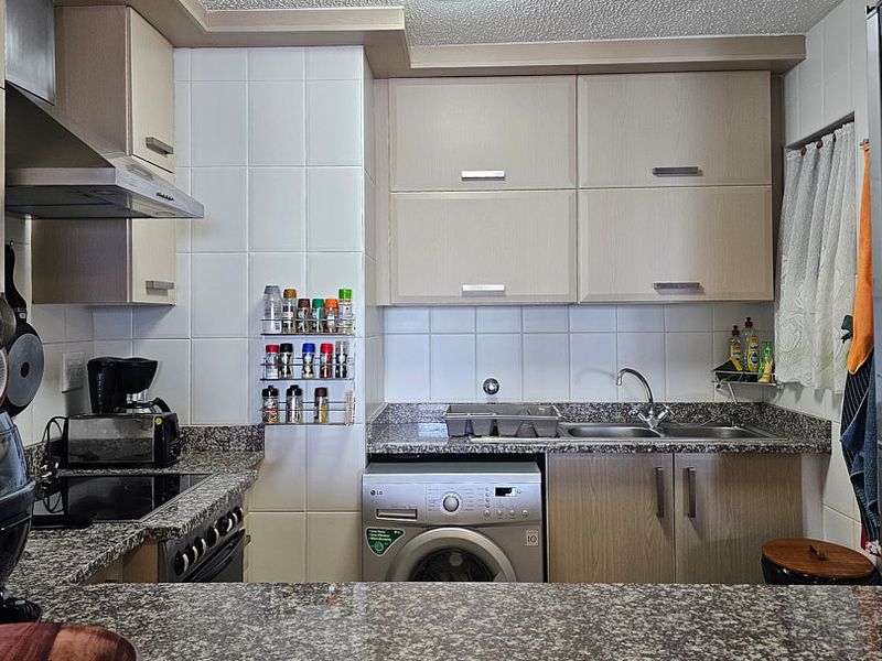 A functional kitchen featuring granite countertops, light wood-finish cabinetry, a tiled backsplash, and an integrated washing machine.