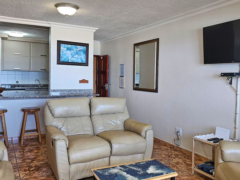 Open plan living area featuring a kitchen with granite countertops and breakfast bar, seamlessly connected to the lounge space with tiled flooring throughout.