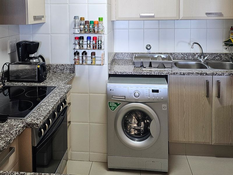 Compact kitchen featuring granite countertops, tiled backsplash, built-in oven, electric hob, and integrated cabinetry with a dedicated space for a washing machine.