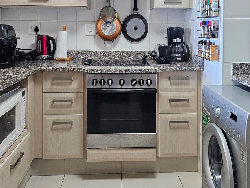 A functional kitchen featuring granite countertops, built-in oven with electric hob, integrated microwave, and ample laminate cabinetry with tiled backsplash and flooring.