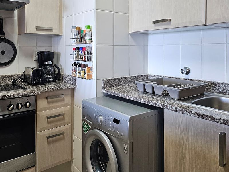 Compact kitchen featuring granite countertops, built-in cabinetry, stainless steel sink, and integrated oven with hob and extractor fan.