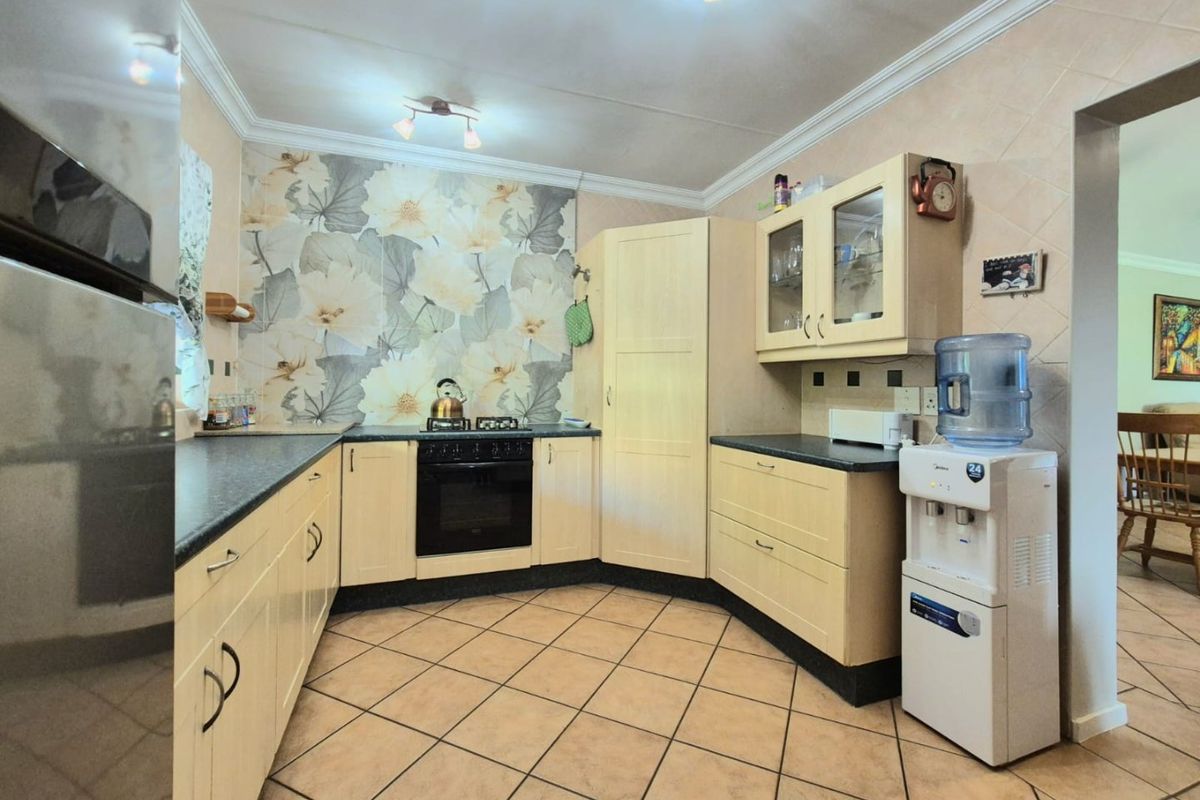 A functional kitchen featuring light-toned cabinetry, dark laminate countertops, a built-in oven and hob, and decorative floral tiled backsplash.