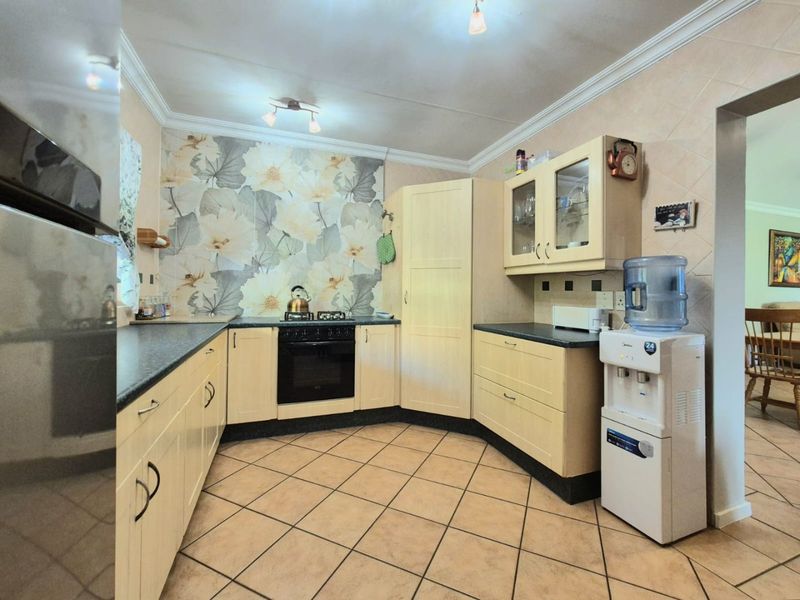 A functional kitchen featuring light-toned cabinetry, dark laminate countertops, a built-in oven and hob, and decorative floral tiled backsplash.