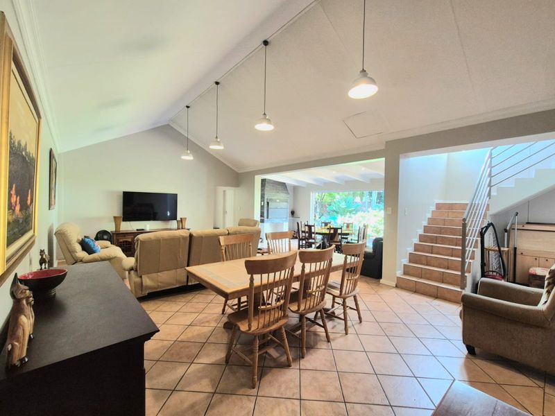 Spacious open-plan living and dining area featuring vaulted ceilings, tiled flooring, and a staircase leading to the upper level with access to a rear patio.