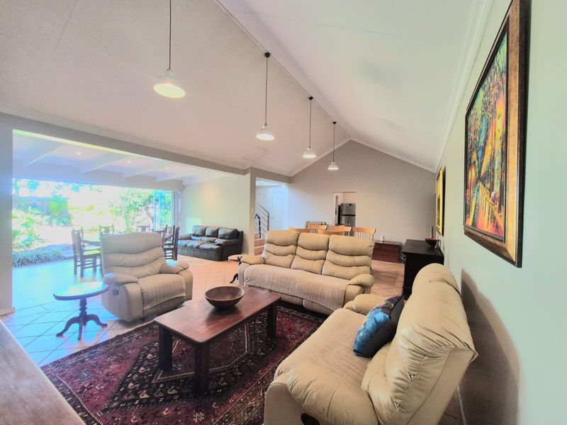 Spacious open-plan living area featuring a high vaulted ceiling, tiled flooring, and large sliding glass doors that open onto an outdoor patio space.
