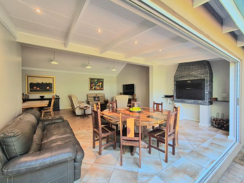 Spacious covered patio featuring a built-in braai, tiled flooring, and exposed ceiling beams, seamlessly connecting to the indoor living area through large sliding doors.