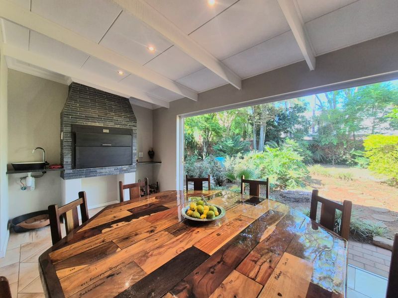 Covered patio featuring a built-in braai, sink, and exposed beam ceiling, with large sliding doors opening onto a lush garden.
