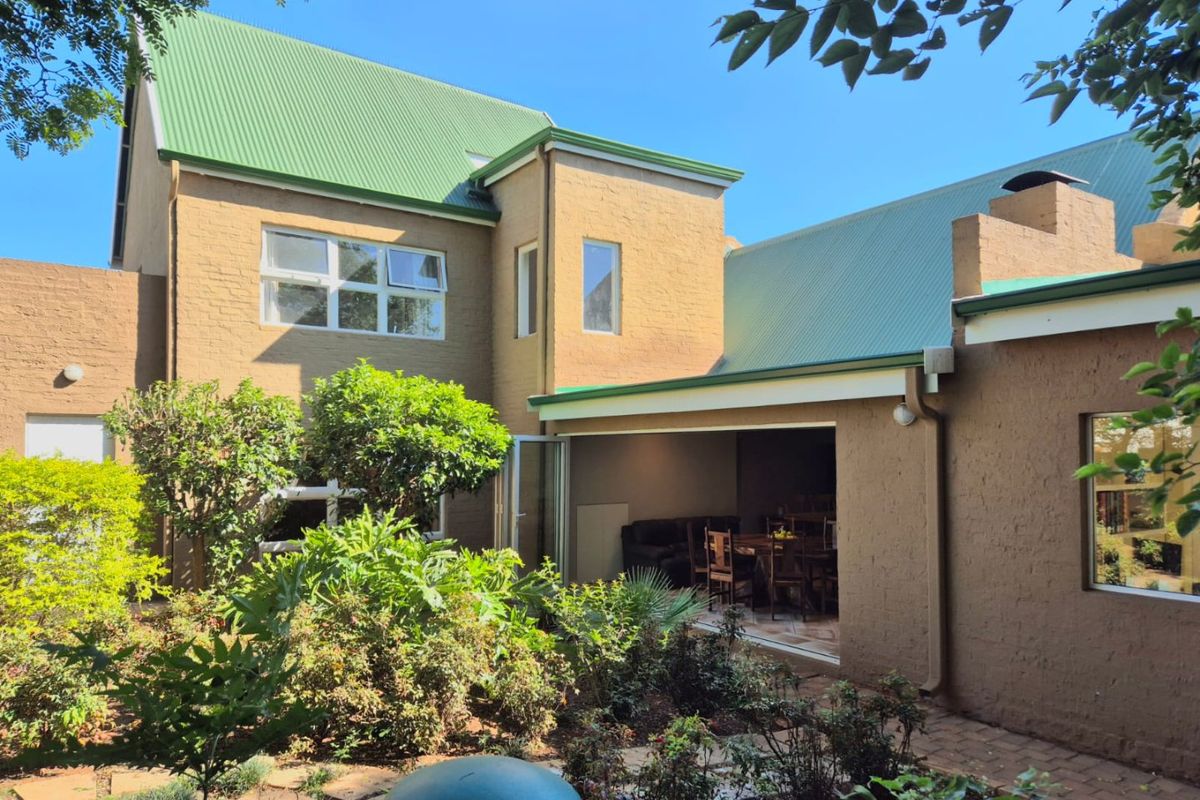 Rear view of a multi-story brick house featuring a green metal roof, paved patio area, and large stacking doors leading into the living space.