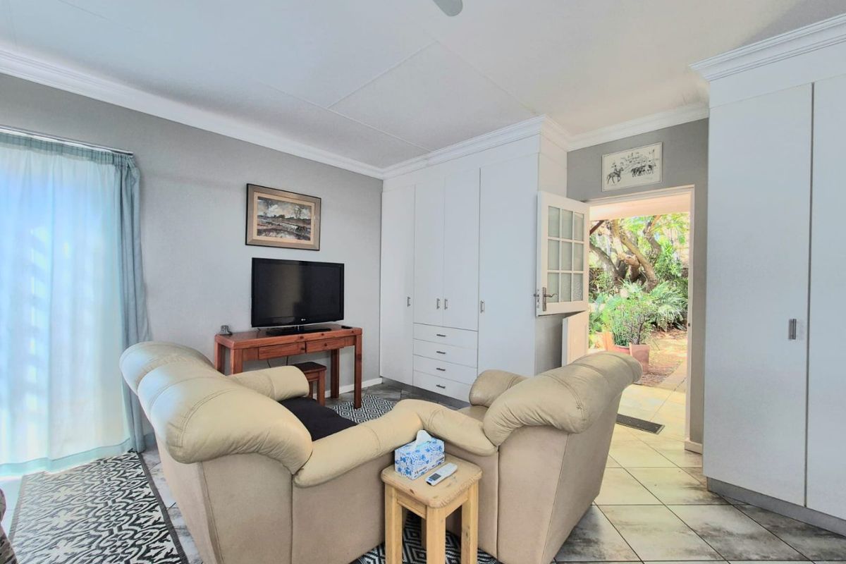 A living room featuring tiled flooring, built-in storage cabinetry, and a ceiling fan, with direct access to an outdoor garden area through a glass door.