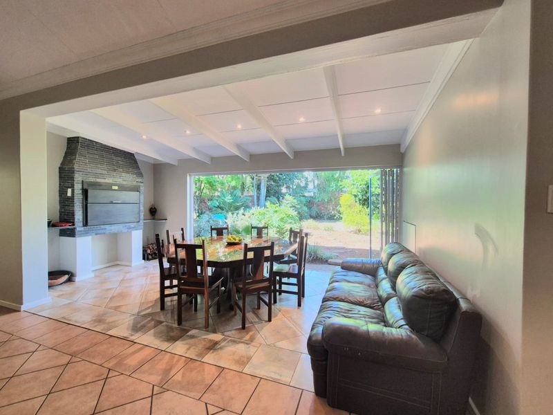 Spacious open-plan living and dining area featuring a built-in fireplace, tiled flooring, exposed beam ceiling, and large stacking doors opening to the garden.
