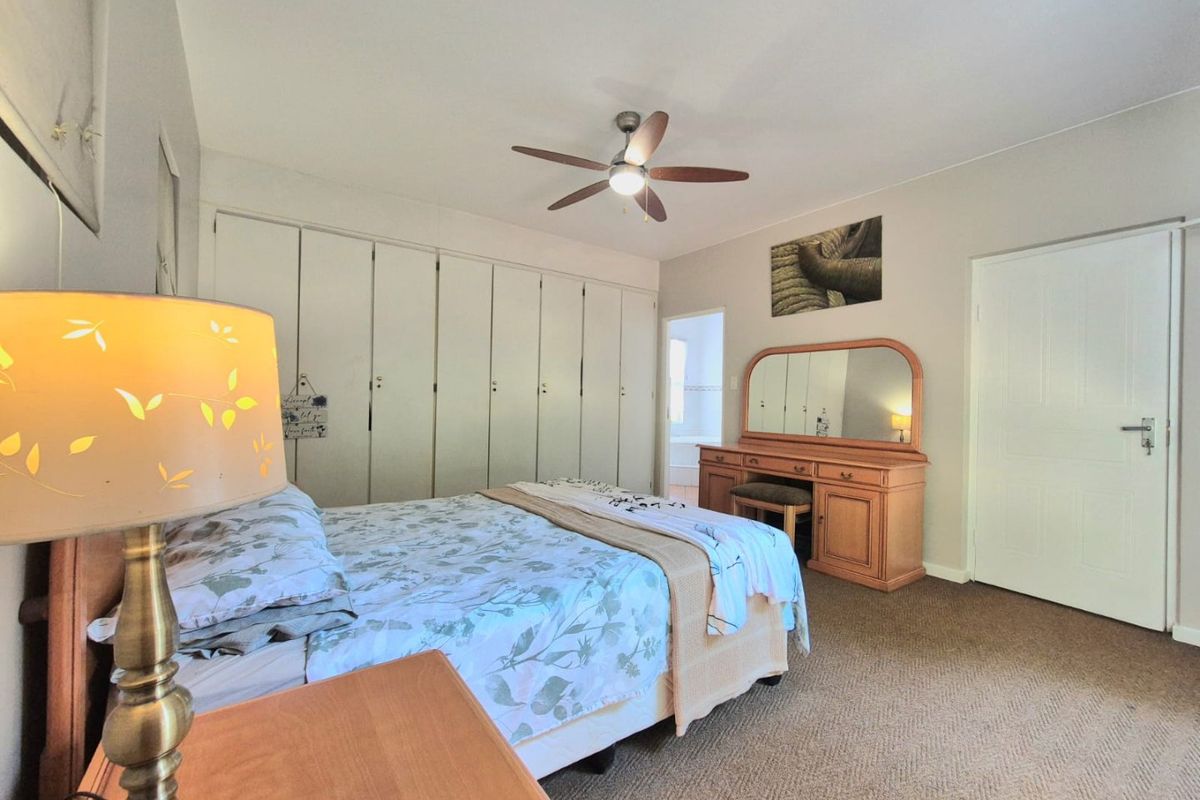 A well-proportioned bedroom featuring extensive built-in cupboard storage, a ceiling fan, and neutral carpeting, with direct access to an adjoining bathroom.