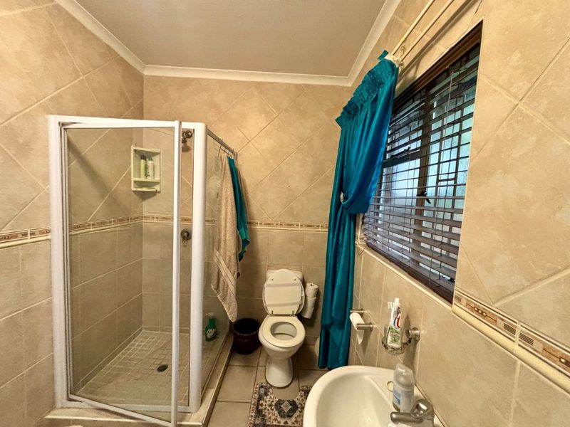 A functional bathroom featuring a shower enclosure, toilet, and pedestal basin with neutral wall and floor tiling.