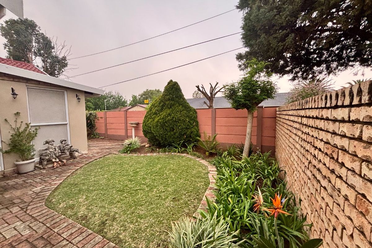 A well-maintained rear garden featuring a paved patio area, established landscaping, and a secure brick boundary wall.