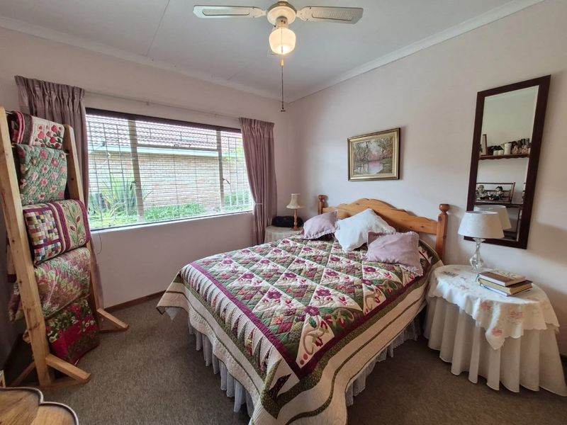 A well-maintained bedroom featuring carpeted flooring, a ceiling fan, and a large window with security bars, offering a comfortable and functional living space.