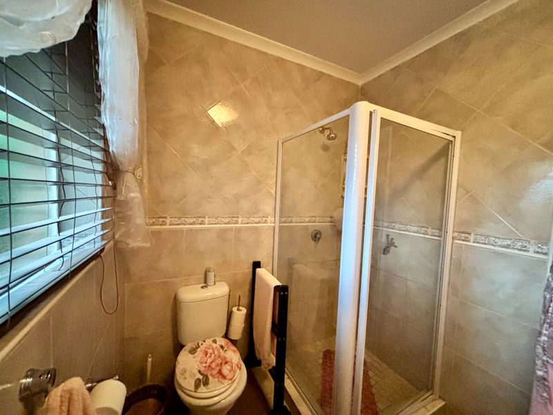 A functional bathroom featuring a glass shower enclosure, toilet, and neutral wall tiling with a decorative border.