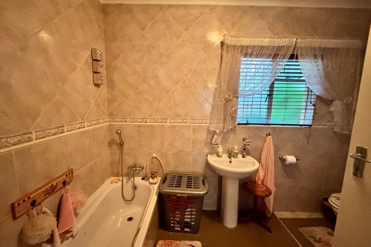 A functional bathroom featuring a pedestal washbasin, built-in bathtub with shower mixer, and tiled wall finishes.