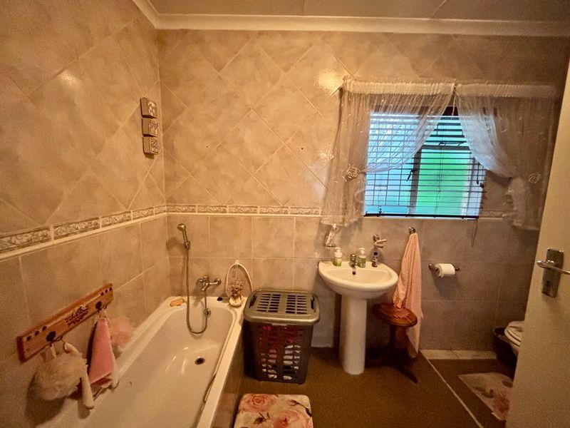 A functional bathroom featuring a pedestal washbasin, built-in bathtub with shower mixer, and tiled wall finishes.