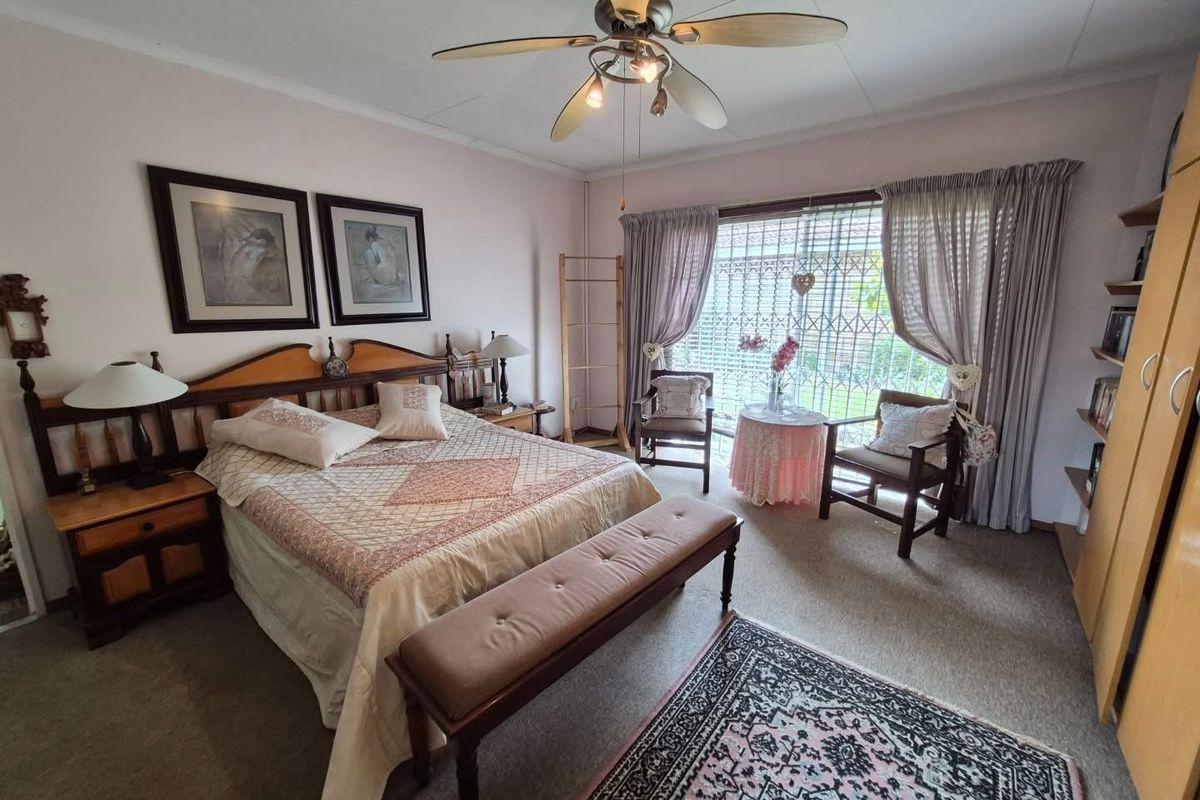 A spacious bedroom featuring built-in cupboards, a ceiling fan, and large windows with security gates, offering a comfortable and functional living space.