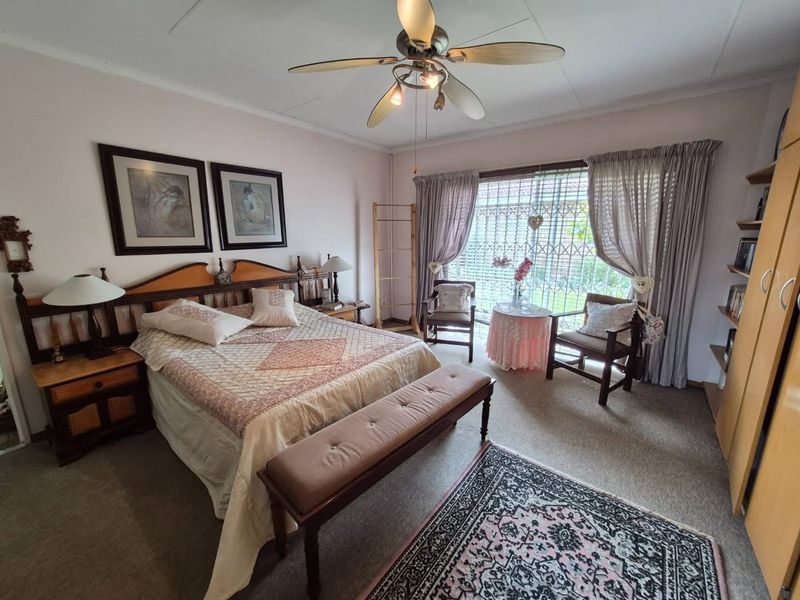 A spacious bedroom featuring built-in cupboards, a ceiling fan, and large windows with security gates, offering a comfortable and functional living space.