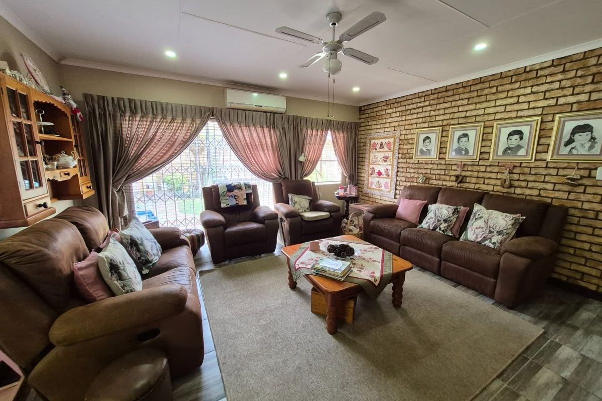A comfortable living room featuring an exposed brick feature wall, tiled flooring, a ceiling fan, and a split-system air conditioner.