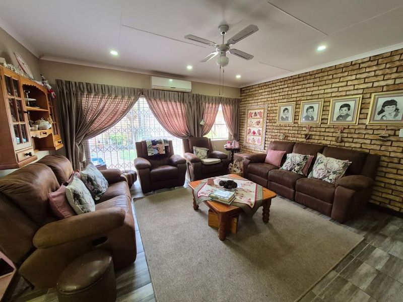 A comfortable living room featuring an exposed brick feature wall, tiled flooring, a ceiling fan, and a split-system air conditioner.