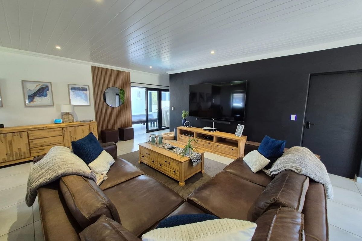 A modern living room featuring a striking black accent wall, timber slat feature paneling, tiled floors, and direct access to an outdoor patio area.
