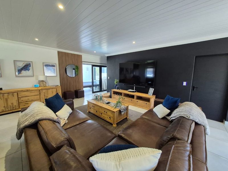 A modern living room featuring a striking black accent wall, timber slat feature paneling, tiled floors, and direct access to an outdoor patio area.