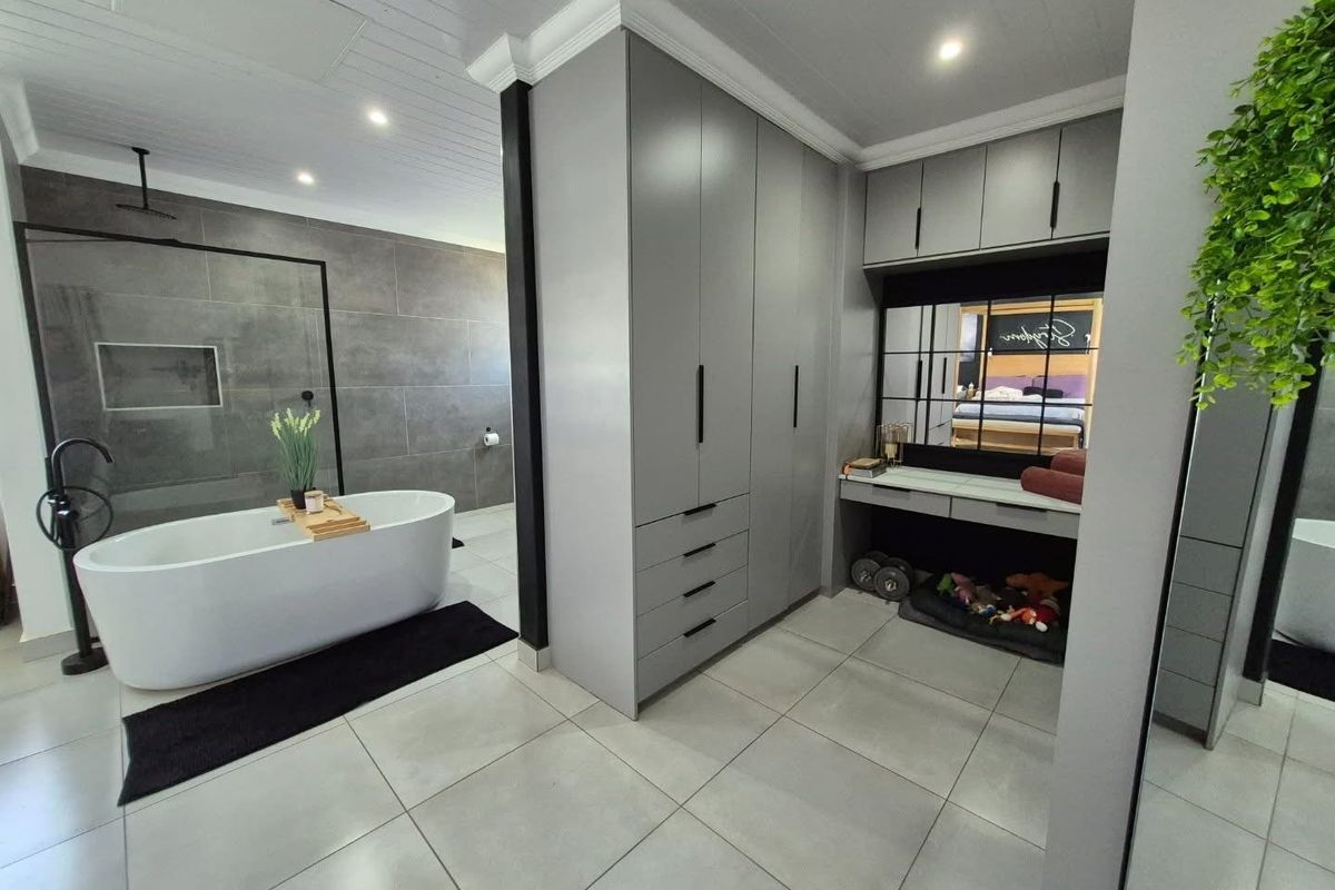 Modern open-plan bathroom featuring a sleek freestanding bathtub, walk-in shower with grey tiling, and extensive built-in cabinetry with a vanity area.