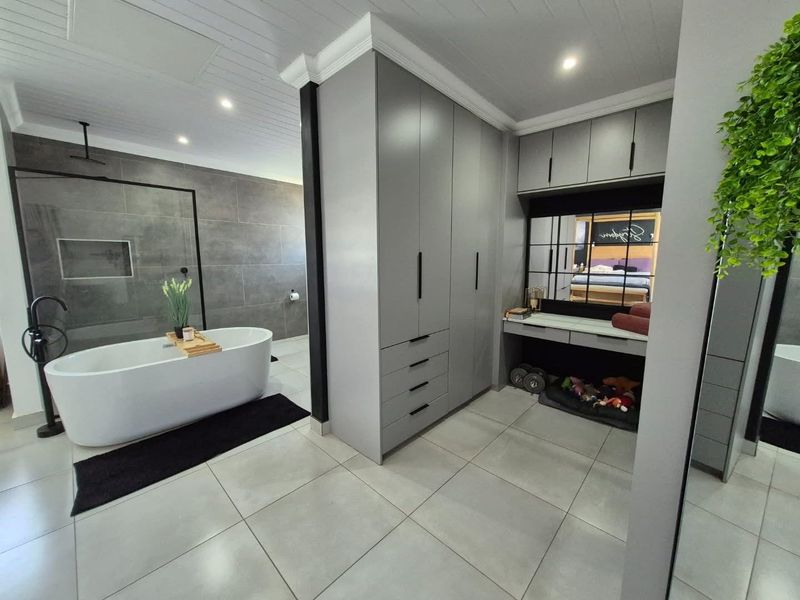 Modern open-plan bathroom featuring a sleek freestanding bathtub, walk-in shower with grey tiling, and extensive built-in cabinetry with a vanity area.