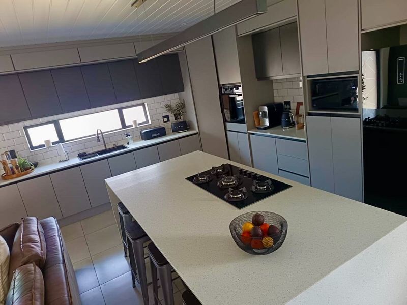 Modern kitchen featuring a large central island with a gas cooktop, sleek cabinetry, stone countertops, and integrated appliances.