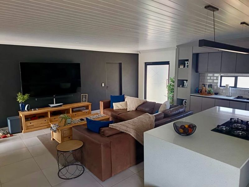 Modern open-plan living area featuring a sleek kitchen with a central island, gas hob, and contemporary cabinetry, seamlessly flowing into the lounge space.