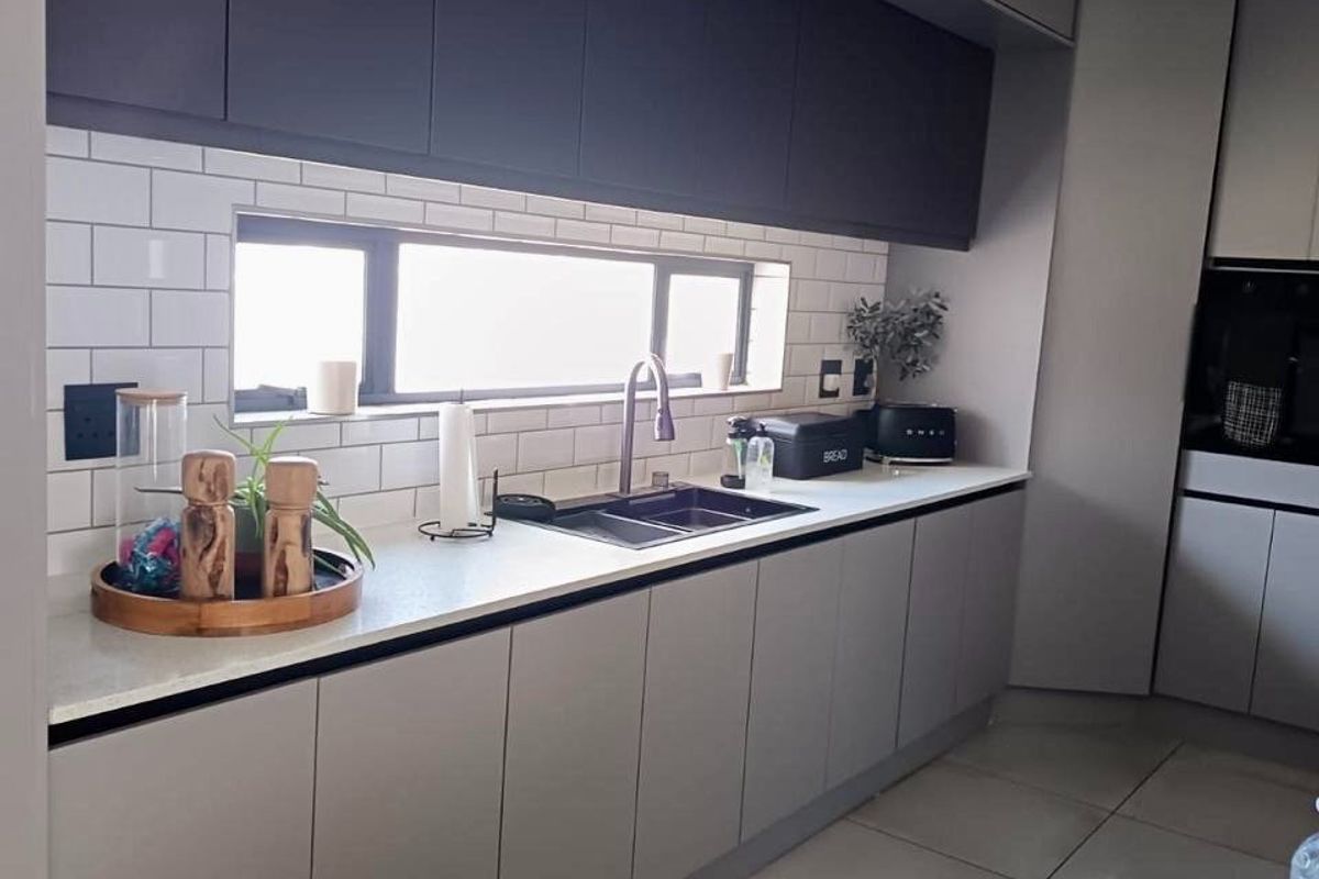 Modern kitchen featuring sleek grey cabinetry, stone countertops, a subway tile backsplash, and high-quality finishes throughout.