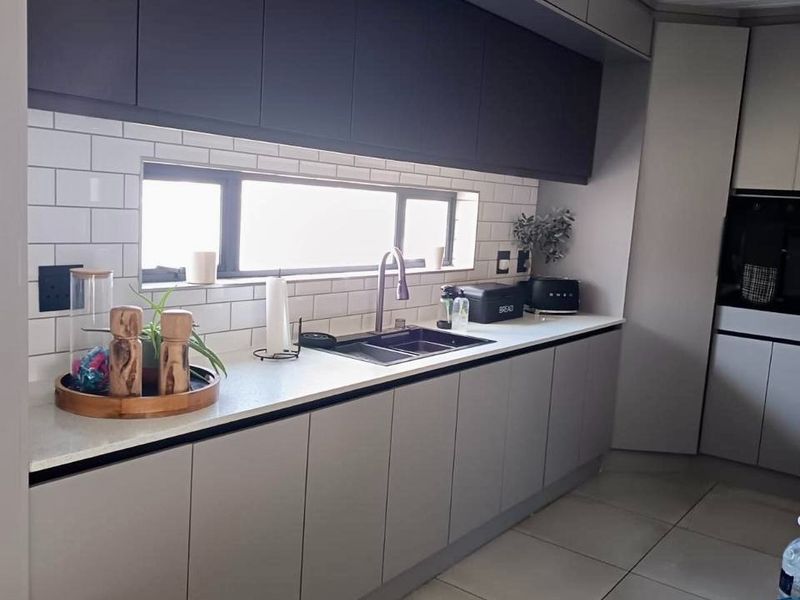 Modern kitchen featuring sleek grey cabinetry, stone countertops, a subway tile backsplash, and high-quality finishes throughout.