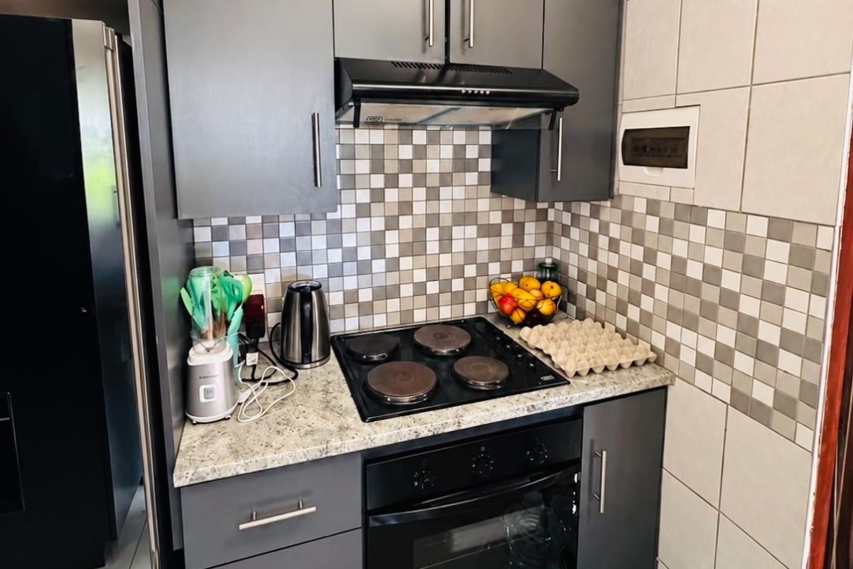 A compact kitchen featuring modern dark grey cabinetry, a granite countertop, an electric hob with an extractor fan, and a tiled backsplash.
