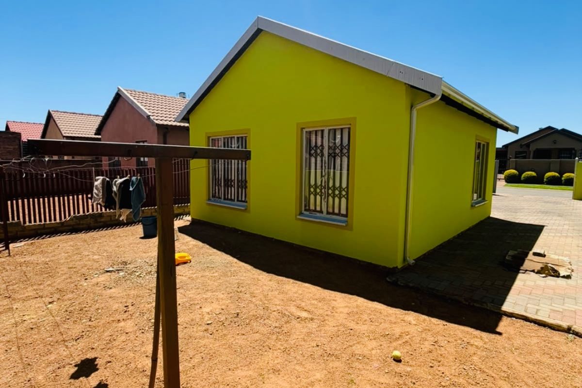 A rear view of a detached house featuring a bright lime-green exterior, security bars on windows, and a paved side walkway.